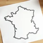 Carte de France vierge imprimée sur feuille A4 posée sur un bureau en bois avec des crayons de couleur
